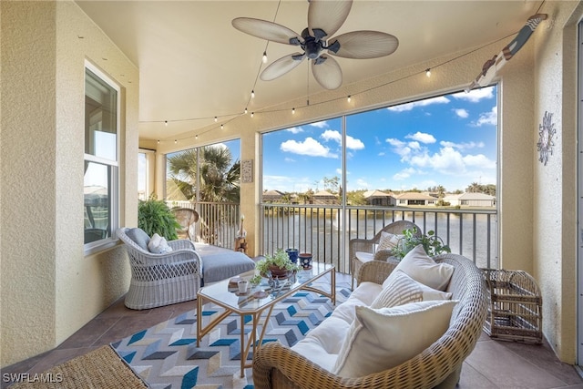 sunroom with ceiling fan and a water view