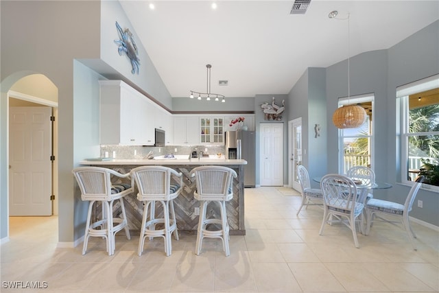 kitchen featuring a kitchen breakfast bar, stainless steel refrigerator with ice dispenser, kitchen peninsula, decorative light fixtures, and white cabinets