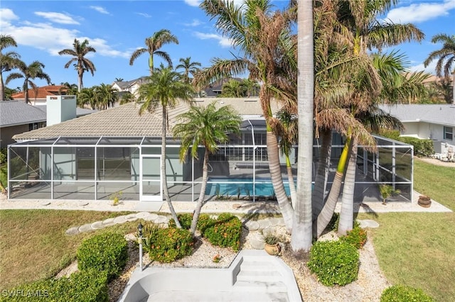 rear view of house with a lanai, a tiled roof, an outdoor pool, and a yard