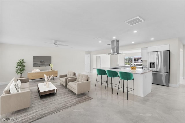 kitchen featuring white cabinetry, stainless steel fridge with ice dispenser, island range hood, ceiling fan, and a breakfast bar