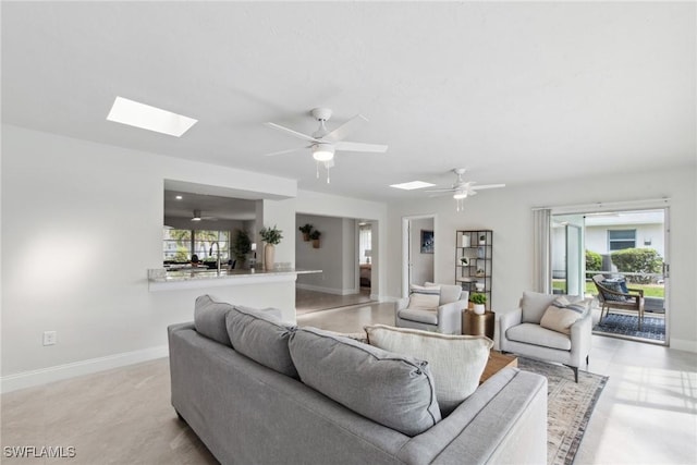 living room featuring a skylight, ceiling fan, baseboards, and a wealth of natural light