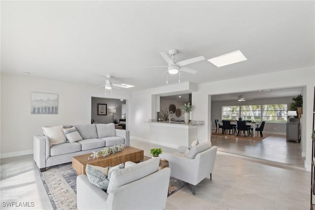 living area with a skylight, baseboards, and a ceiling fan