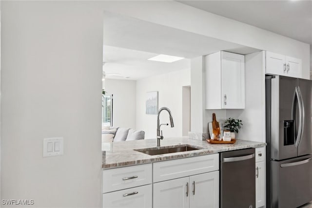 kitchen with light stone counters, stainless steel appliances, a sink, a ceiling fan, and white cabinets