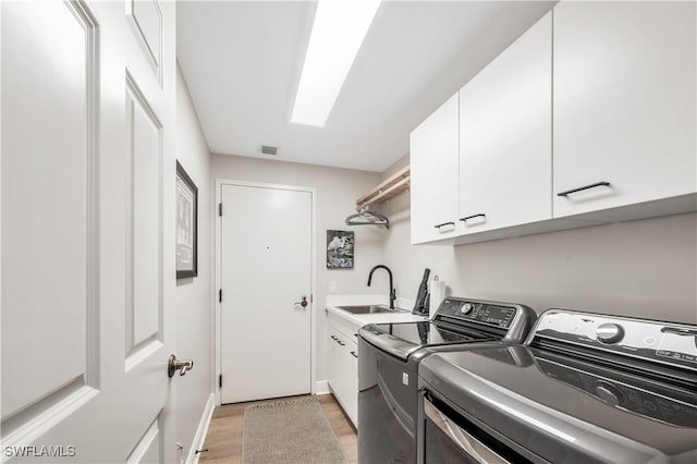 laundry room featuring cabinets, washer and clothes dryer, sink, and light hardwood / wood-style floors