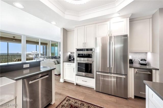 kitchen with stainless steel appliances, a raised ceiling, light hardwood / wood-style flooring, and white cabinets