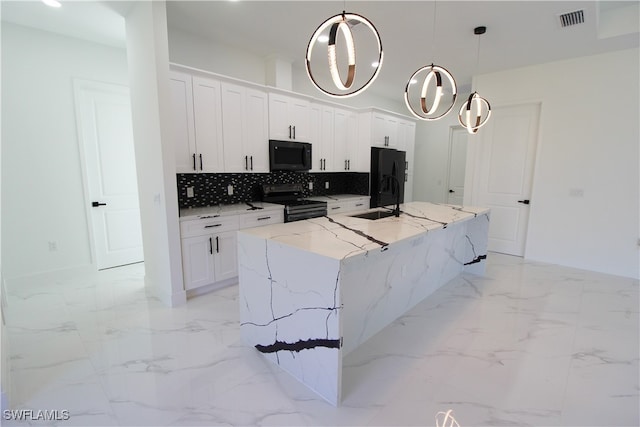 kitchen featuring light stone counters, a kitchen island with sink, black appliances, decorative light fixtures, and white cabinets