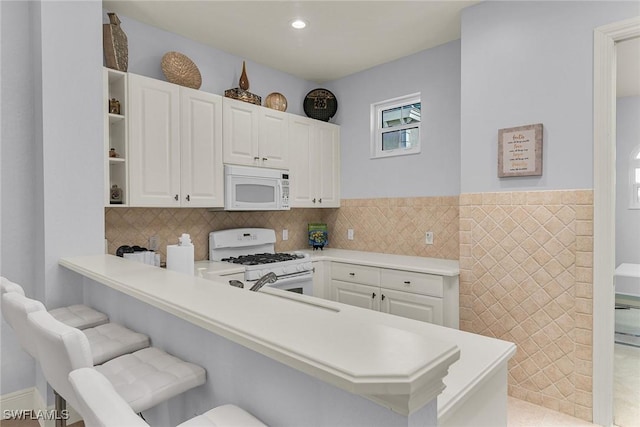 kitchen with white appliances, white cabinetry, sink, kitchen peninsula, and a breakfast bar area