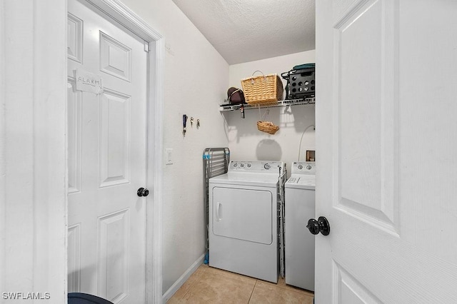 clothes washing area with laundry area, light tile patterned floors, baseboards, washer and dryer, and a textured ceiling