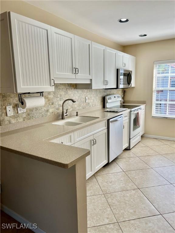 kitchen featuring sink, light tile patterned floors, appliances with stainless steel finishes, white cabinetry, and kitchen peninsula