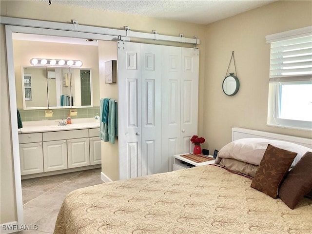 bedroom with light tile patterned flooring, ensuite bath, sink, a textured ceiling, and a closet