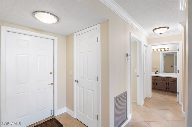 corridor with sink, a textured ceiling, ornamental molding, and light tile patterned flooring