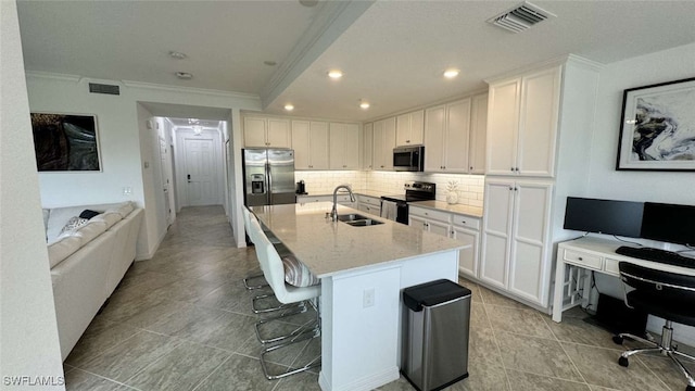 kitchen with light stone countertops, appliances with stainless steel finishes, sink, white cabinets, and an island with sink