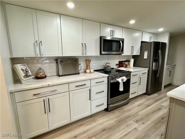 kitchen featuring light stone countertops, tasteful backsplash, stainless steel appliances, light hardwood / wood-style floors, and white cabinetry