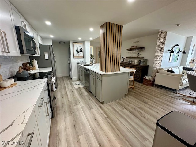 kitchen featuring light stone countertops, stainless steel appliances, backsplash, light hardwood / wood-style floors, and white cabinets