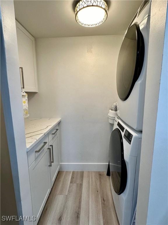 laundry area with cabinets, light hardwood / wood-style floors, and stacked washer and clothes dryer