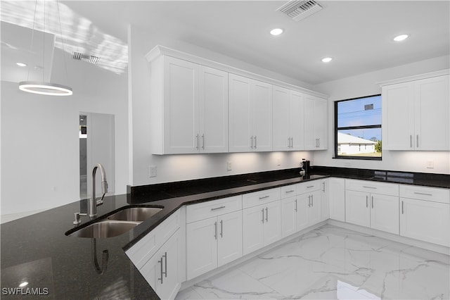 kitchen with dark stone countertops, white cabinetry, and sink