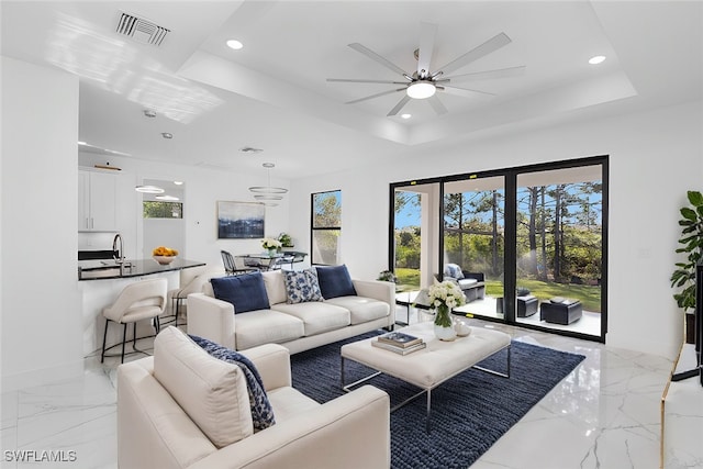 living room featuring ceiling fan, sink, and a tray ceiling