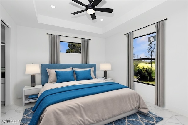 bedroom featuring a raised ceiling, multiple windows, and ceiling fan