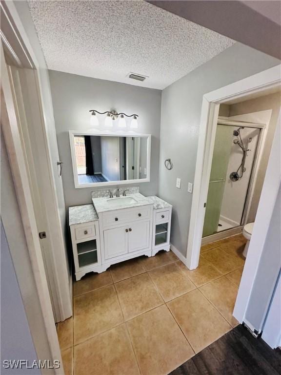 bathroom with a textured ceiling, tile patterned floors, vanity, and a shower with shower door