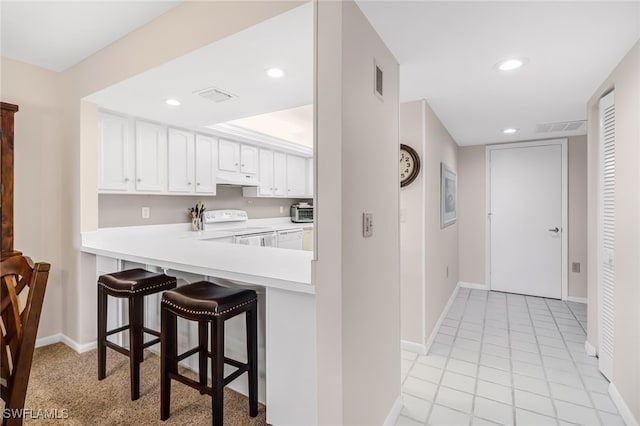 kitchen with white cabinets, light tile patterned floors, white range with electric stovetop, a kitchen bar, and kitchen peninsula