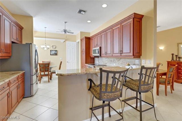 kitchen with a kitchen breakfast bar, tasteful backsplash, decorative light fixtures, ceiling fan with notable chandelier, and appliances with stainless steel finishes