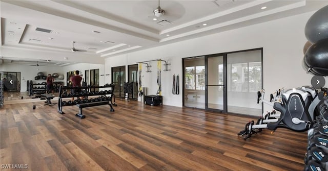 workout area with ceiling fan, dark hardwood / wood-style floors, and a raised ceiling