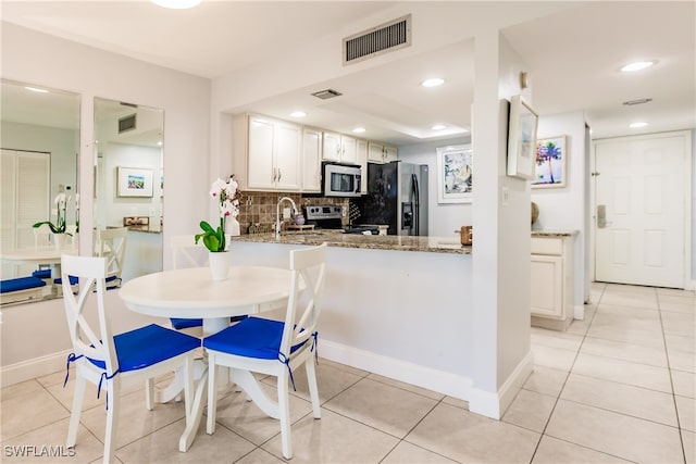 kitchen featuring kitchen peninsula, appliances with stainless steel finishes, backsplash, stone counters, and white cabinetry