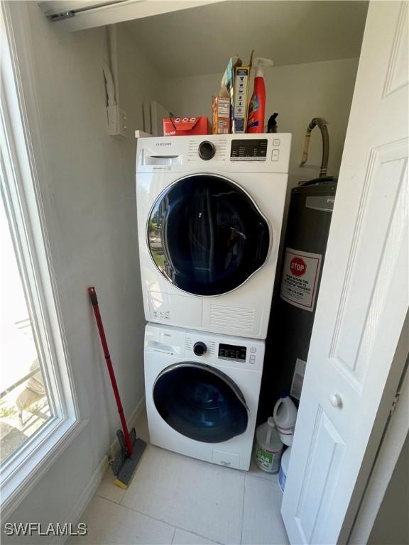 washroom with electric water heater, stacked washing maching and dryer, and light tile patterned flooring