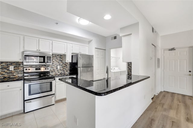 kitchen with washing machine and clothes dryer, stainless steel appliances, kitchen peninsula, light hardwood / wood-style floors, and white cabinets