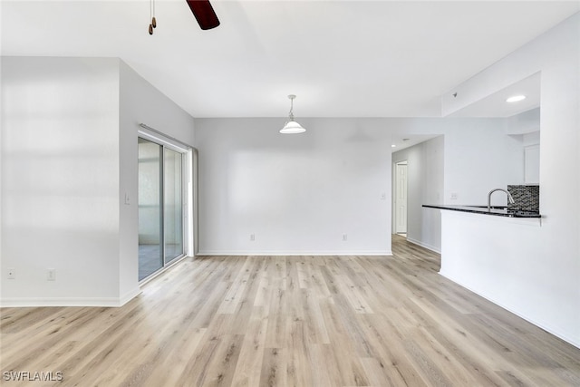 unfurnished living room featuring light wood-type flooring, ceiling fan, and sink