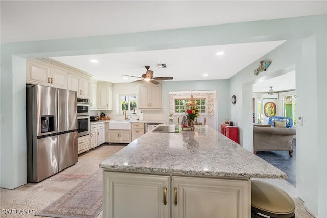 kitchen with appliances with stainless steel finishes, sink, a kitchen breakfast bar, light stone countertops, and cream cabinetry