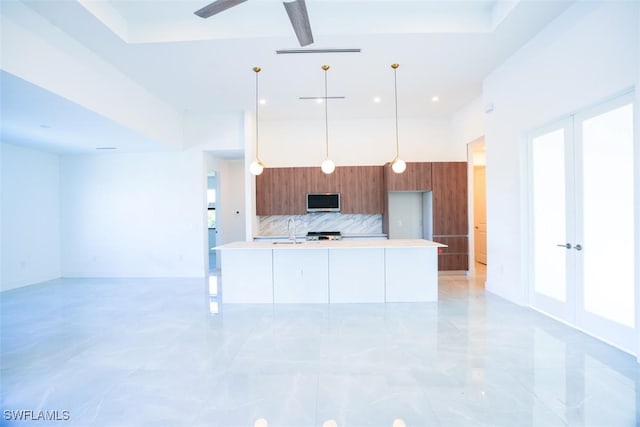 kitchen with ceiling fan, sink, hanging light fixtures, backsplash, and a kitchen island with sink