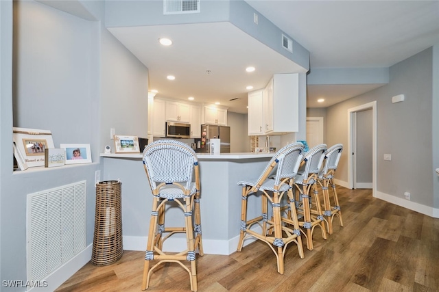 kitchen featuring hardwood / wood-style floors, white cabinetry, kitchen peninsula, and appliances with stainless steel finishes