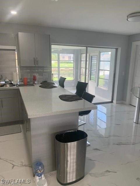 kitchen with tasteful backsplash, gray cabinetry, light stone countertops, and a kitchen bar