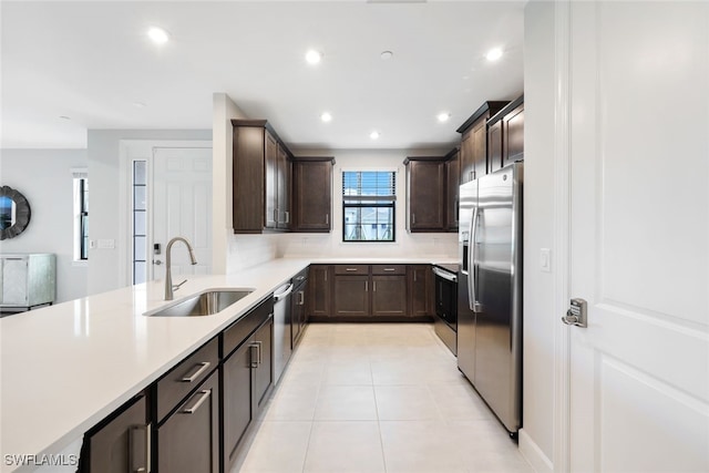 kitchen with appliances with stainless steel finishes, light tile patterned floors, dark brown cabinets, and sink