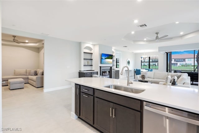 kitchen featuring stainless steel dishwasher, ceiling fan with notable chandelier, dark brown cabinetry, a raised ceiling, and sink