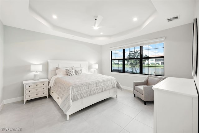 bedroom with ceiling fan, a water view, light tile patterned floors, and a tray ceiling