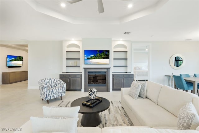 living room featuring a raised ceiling, built in shelves, and ceiling fan