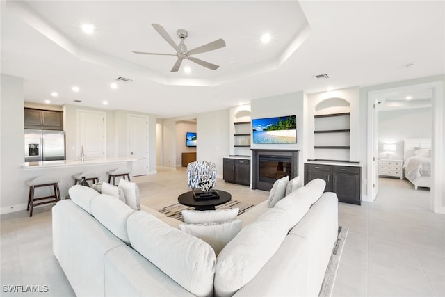 tiled living room featuring a tray ceiling, ceiling fan, and built in features