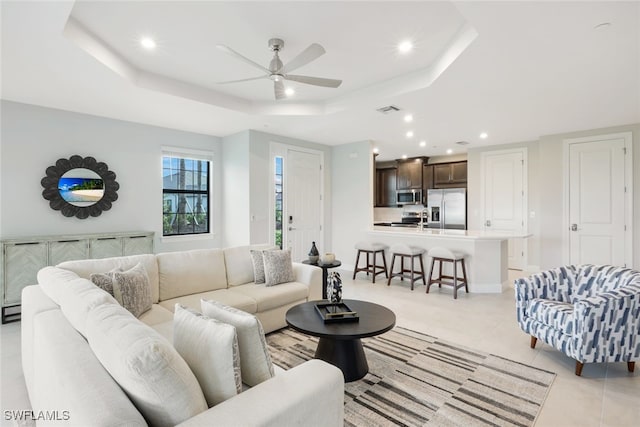 living room featuring light tile patterned floors, a raised ceiling, and ceiling fan