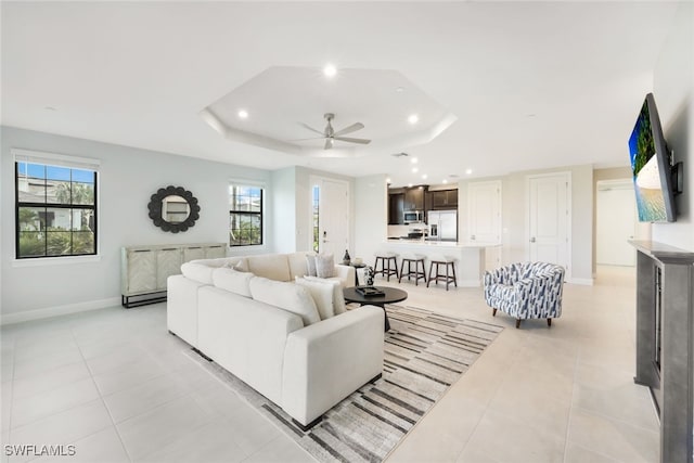 tiled living room with plenty of natural light, ceiling fan, and a raised ceiling