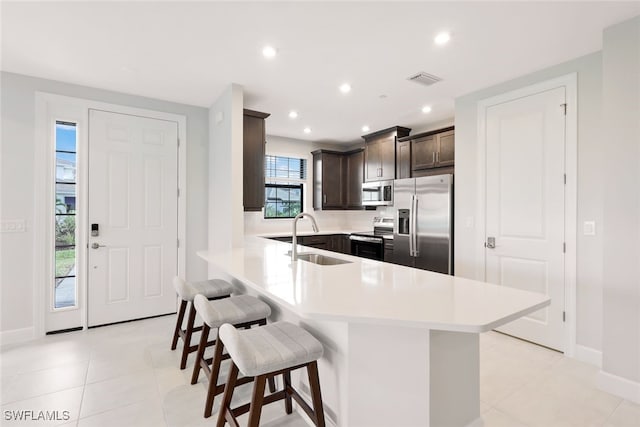 kitchen featuring sink, appliances with stainless steel finishes, light tile patterned flooring, a kitchen bar, and kitchen peninsula