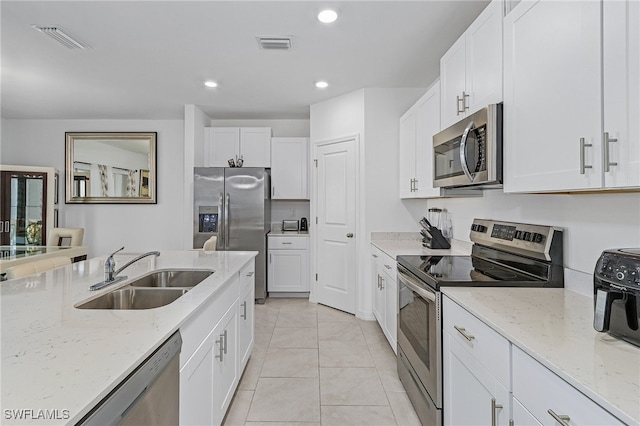 kitchen featuring appliances with stainless steel finishes, light stone counters, sink, light tile patterned floors, and white cabinetry