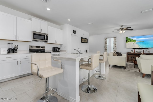 kitchen featuring appliances with stainless steel finishes, a breakfast bar, ceiling fan, a center island with sink, and white cabinets