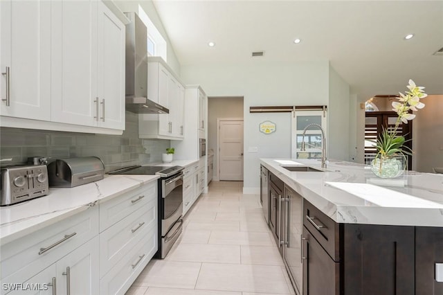 kitchen with white cabinetry, sink, wall chimney exhaust hood, a barn door, and stainless steel electric stove