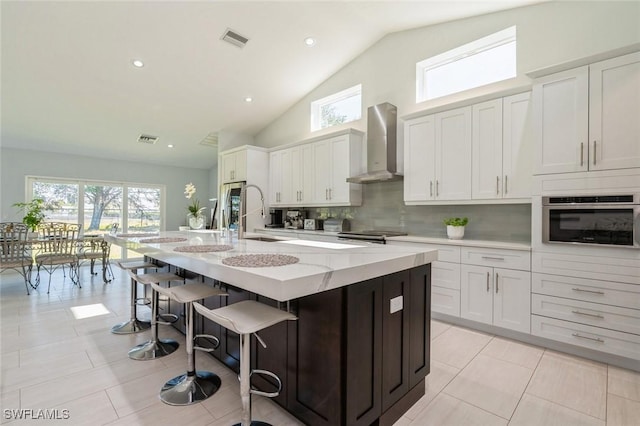 kitchen with white cabinets, sink, wall chimney exhaust hood, an island with sink, and stainless steel appliances