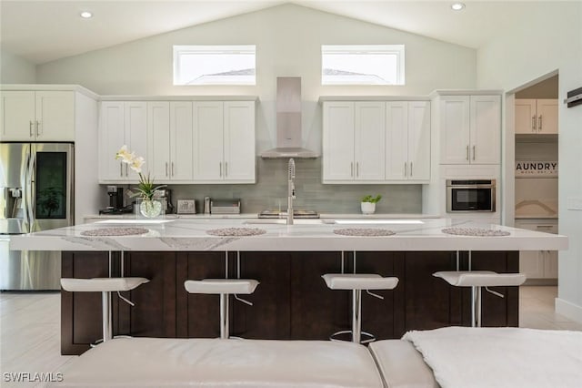 kitchen featuring a breakfast bar area, white cabinets, wall chimney exhaust hood, and appliances with stainless steel finishes