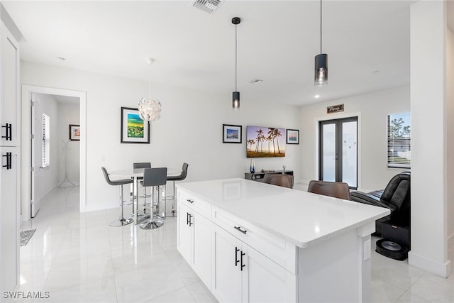 kitchen with french doors, pendant lighting, a notable chandelier, a center island, and white cabinetry