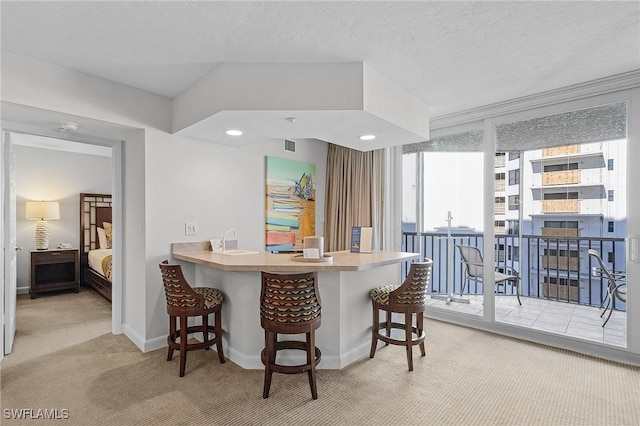 kitchen featuring a textured ceiling, a kitchen bar, light colored carpet, and kitchen peninsula