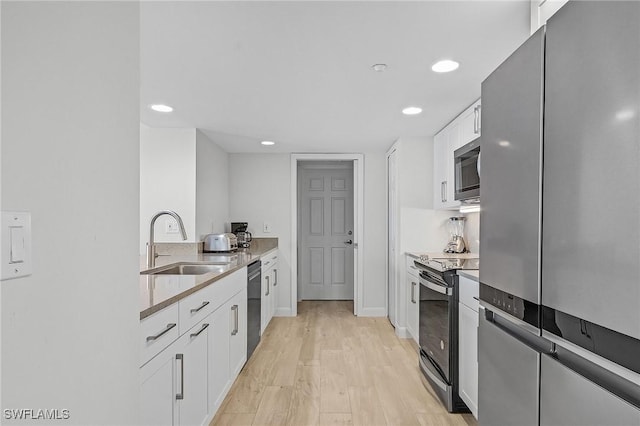 kitchen featuring white cabinetry, sink, light stone counters, appliances with stainless steel finishes, and light wood-type flooring